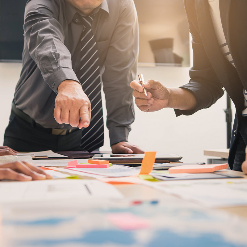 Personas señalando ideas en una mesa de trabajo, representando un proceso colaborativo de innovación estratégica.